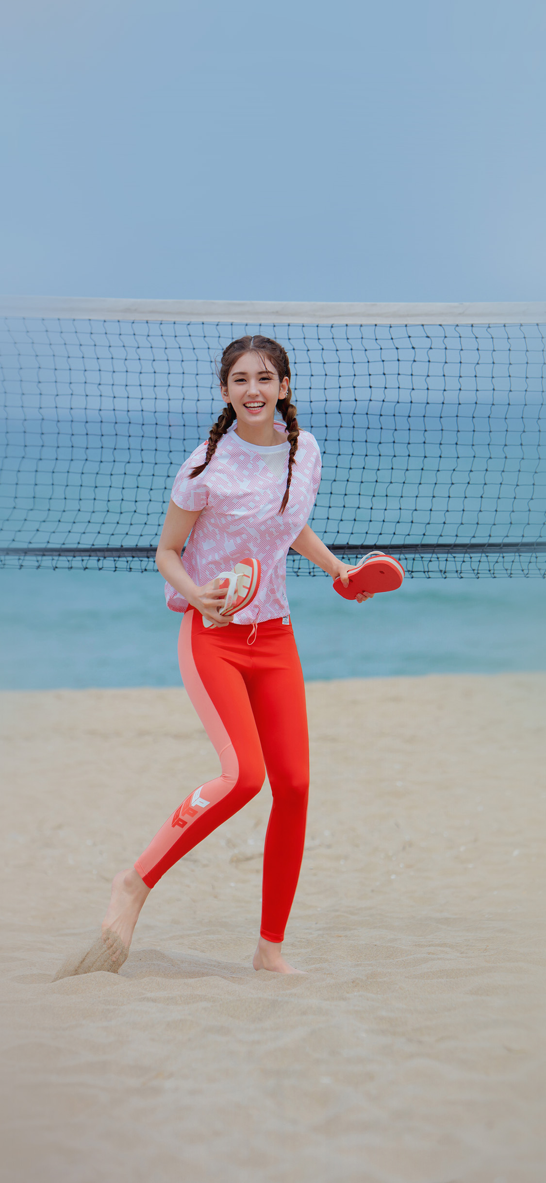 沙滩上穿红色运动裤开心玩沙滩排球的美女高清手机壁纸